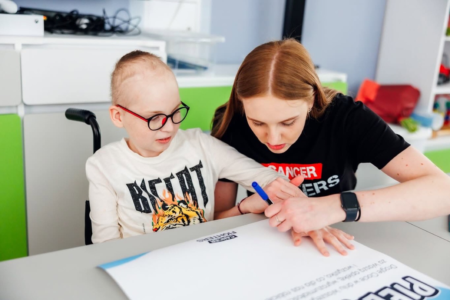 Wolontariuszka Cancer Fighters rysuje razem z dzieckiem przy stoliku na oddziale